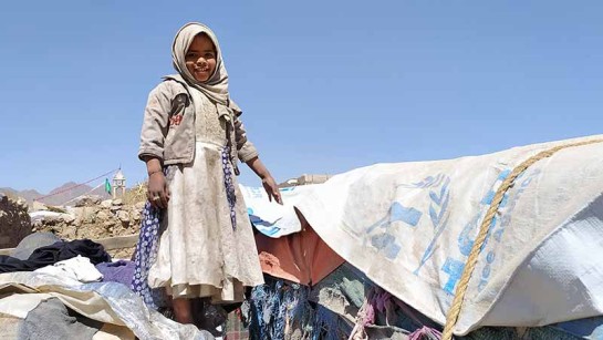 Sumaya, 7 år, står utanför sitt tält. Hon och hennes familj har tvingats fly från strider. Som många andra kämpar de för att överleva.